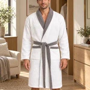 Bata de toalla blanca Giomus con detalles grises, en una escena de uso en casa con modelo masculino adulto. Visualización con IA.