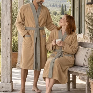 Pareja adulta con batas Giomus camel y ribetes grises en un porche de campo. Escena ilustrativa creada con IA.