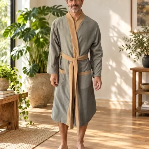 Bata de microfibra gris con cuello, cinturón y ribetes marrones sobre modelo masculino adulto en sala de plantas. Visualización con IA basada en la prenda original.